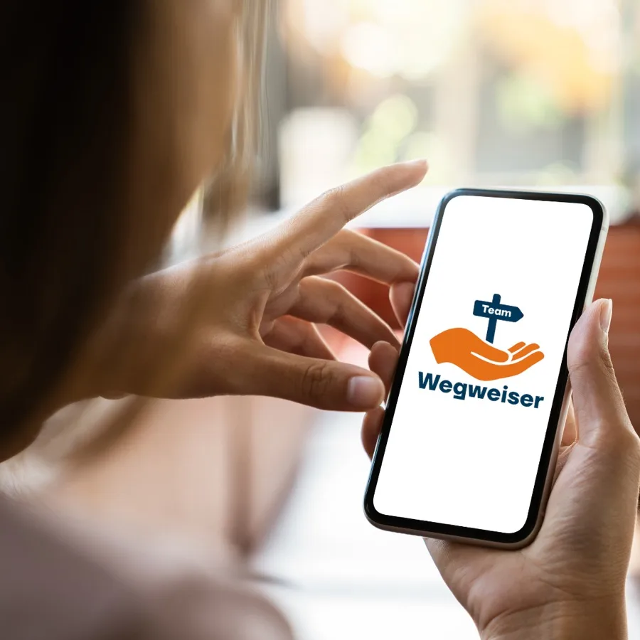 Person hält ein Smartphone mit dem Team-Wegweiser-Logo