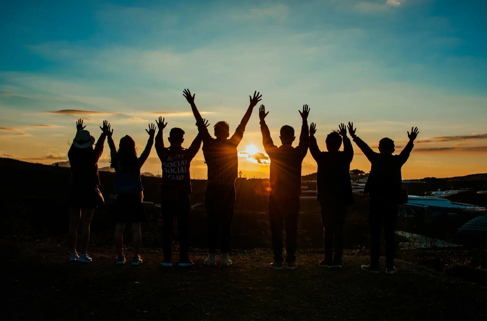 Gruppe junger Menschen hebt bei Sonnenuntergang gemeinsam die Arme